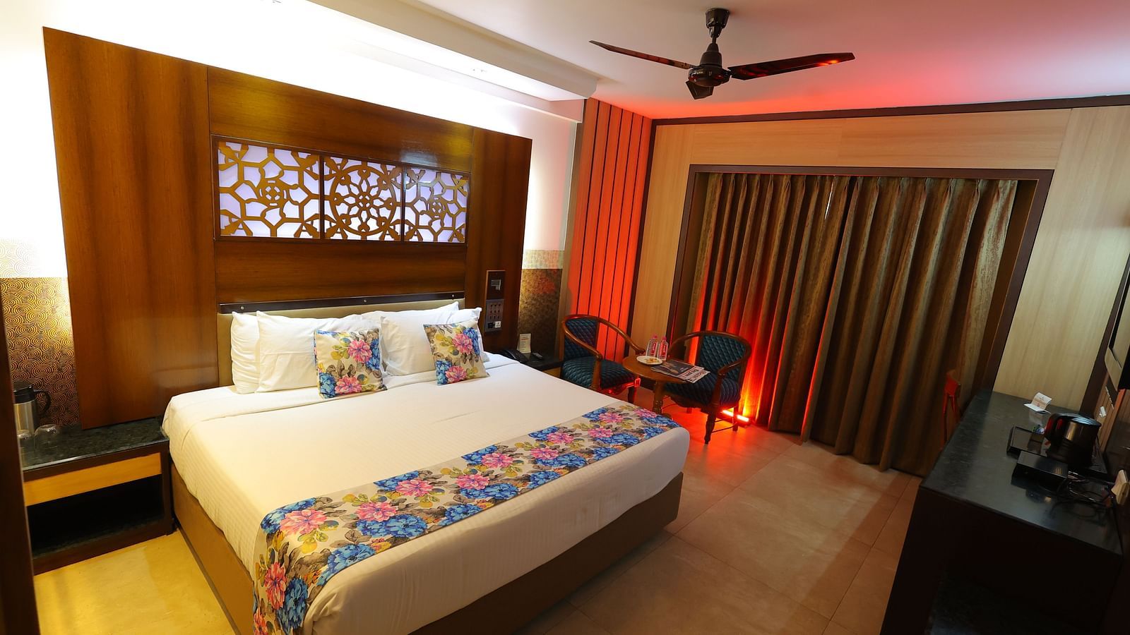  Overview image of a deluxe room at Hotel Amar with a bed, table, TV and huge window with curtains. 