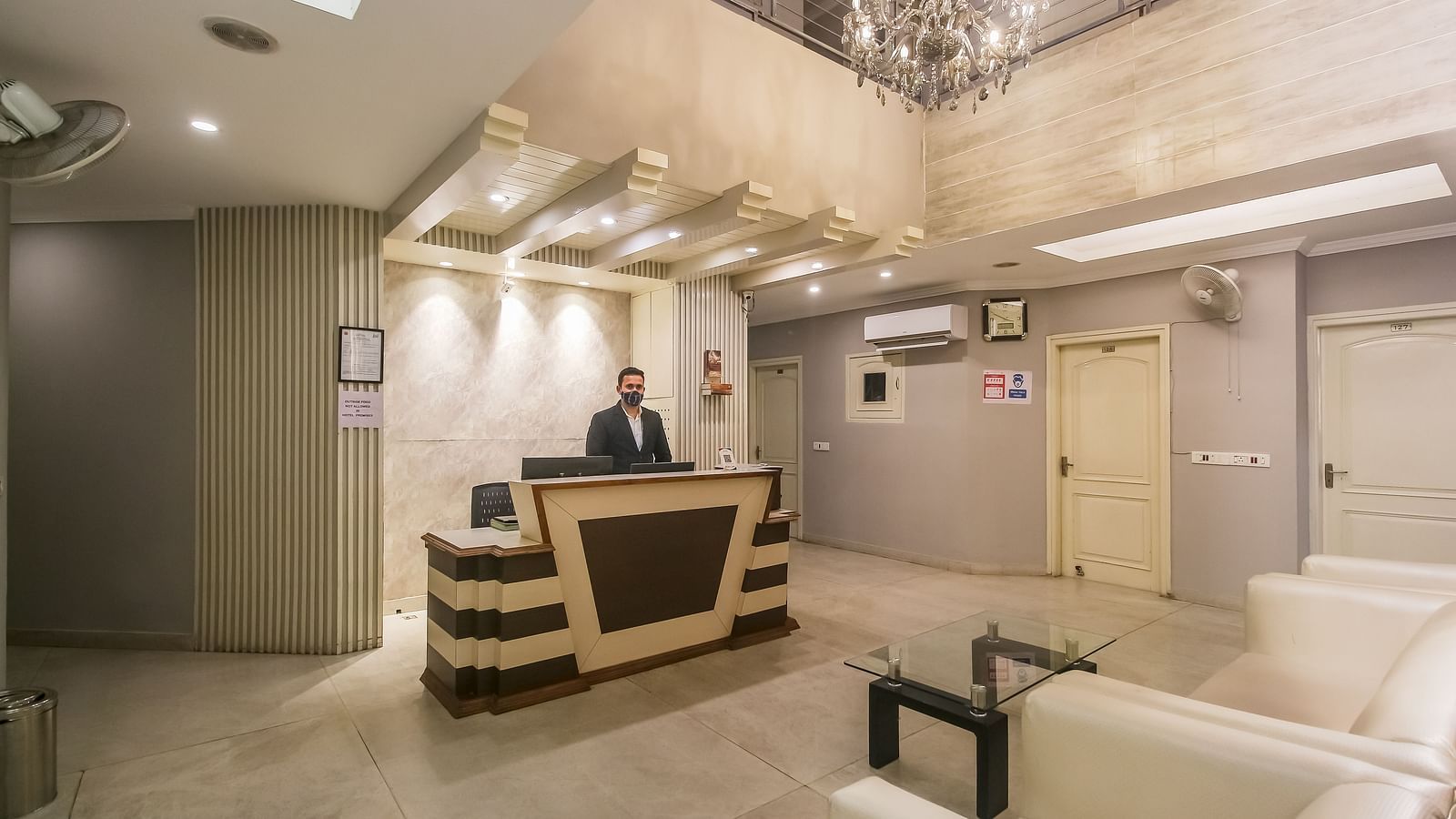 A hotel lobby with a reception desk, a chandelier, a seating area with white sofas, and a staff member behind the counter, lit by soft lighting. - Hotel Diamond Plaza, Chandigarh.