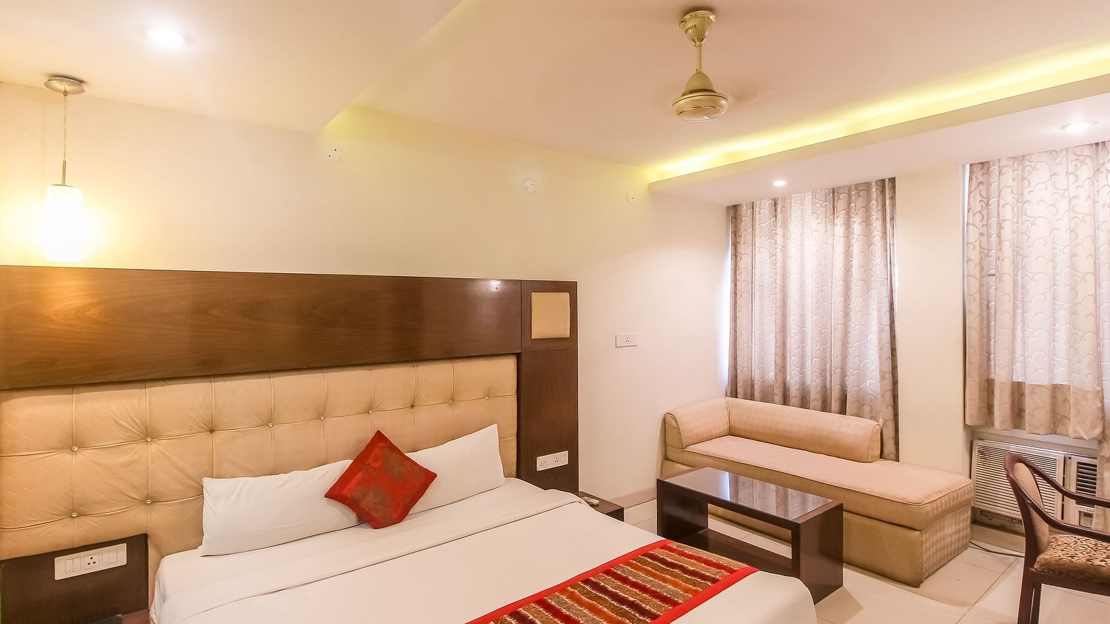 A cosy hotel room with a plush bed, a small sofa, and a glass-topped table. - Hotel Diamond Plaza, Chandigarh.