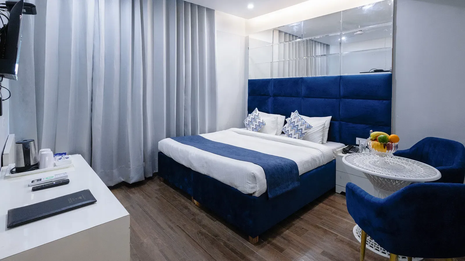 Deluxe Room featuring a king size bed with a blue headboard and white and blue linens, two blue chairs with a small round table, and light wood-look flooring. - Hotel Downtown17, Chandigarh