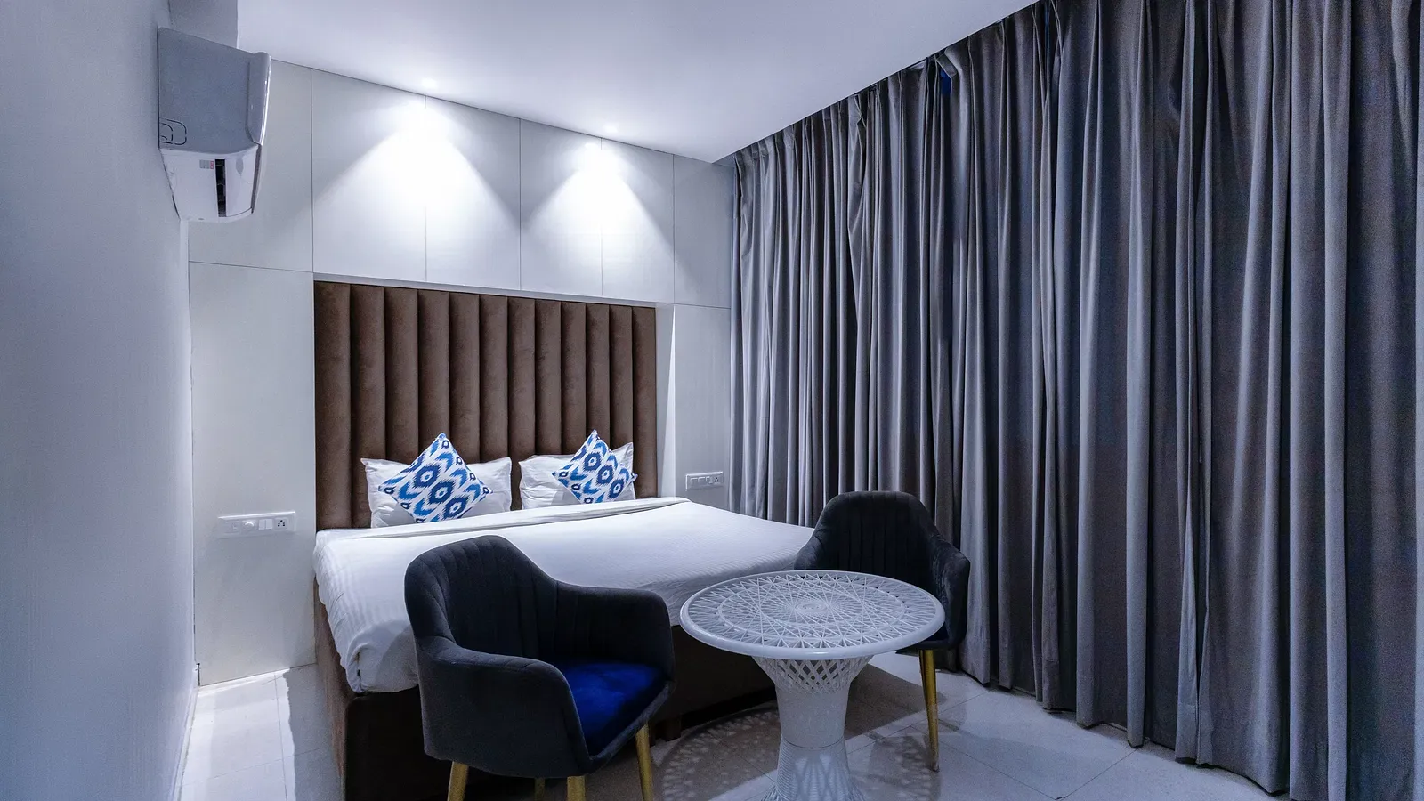Deluxe Room featuring a king size bed with patterned cushions, two chairs, a table, and curtains. - Hotel Downtown17, Chandigarh