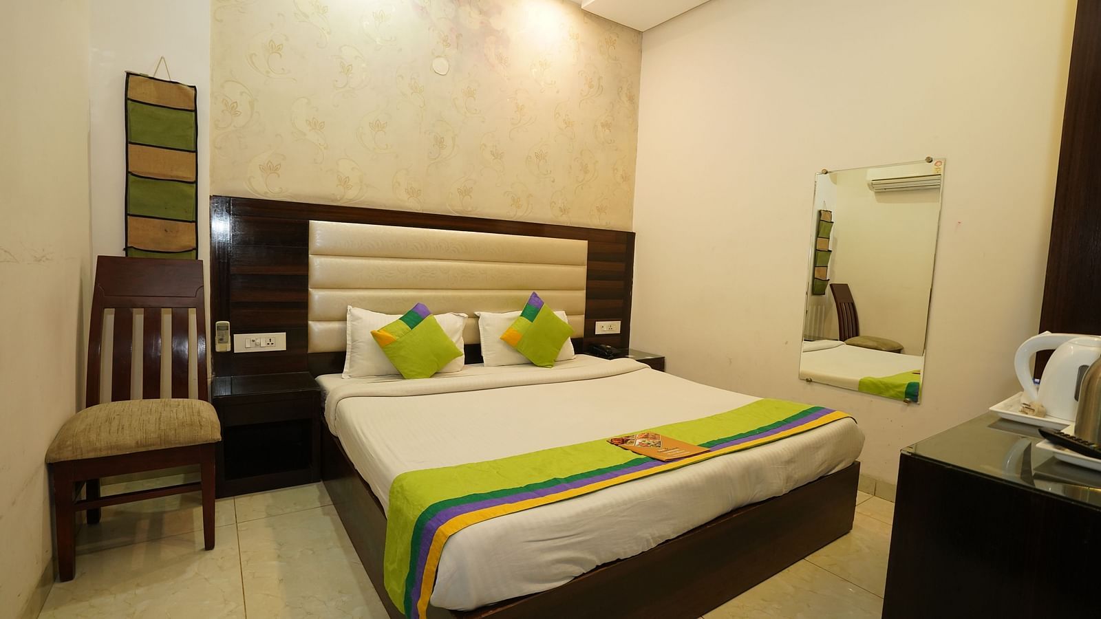 Standard Room featuring a double bed with green-accented linens and pillows, a wooden chair, a dark-wood headboard, and a bedside table with a kettle. - Hotel Dreamland, Chandigarh
