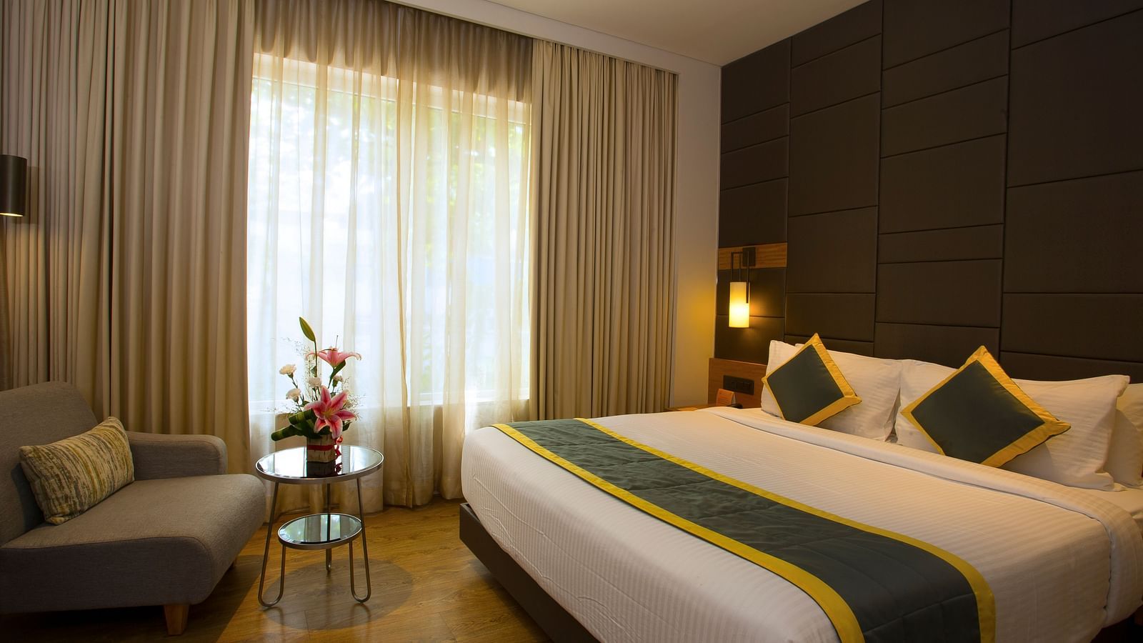 a bedroom with a large bed and a sofa opposite the the bed, with a small table in the middle - Hotel Fountain Tree By TGI - JP Nagar, Bangalore