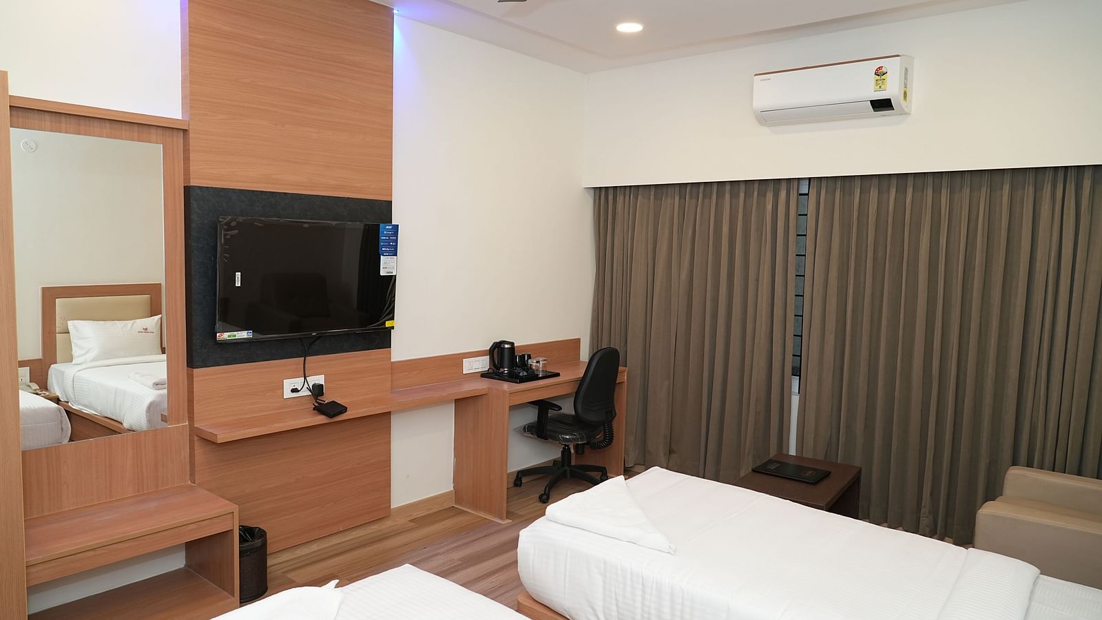 a bedroom with modern furnishings featuring a twin bed along with a medium mirror and a wall mounted television opposite to it - Hotel Grand Sigma