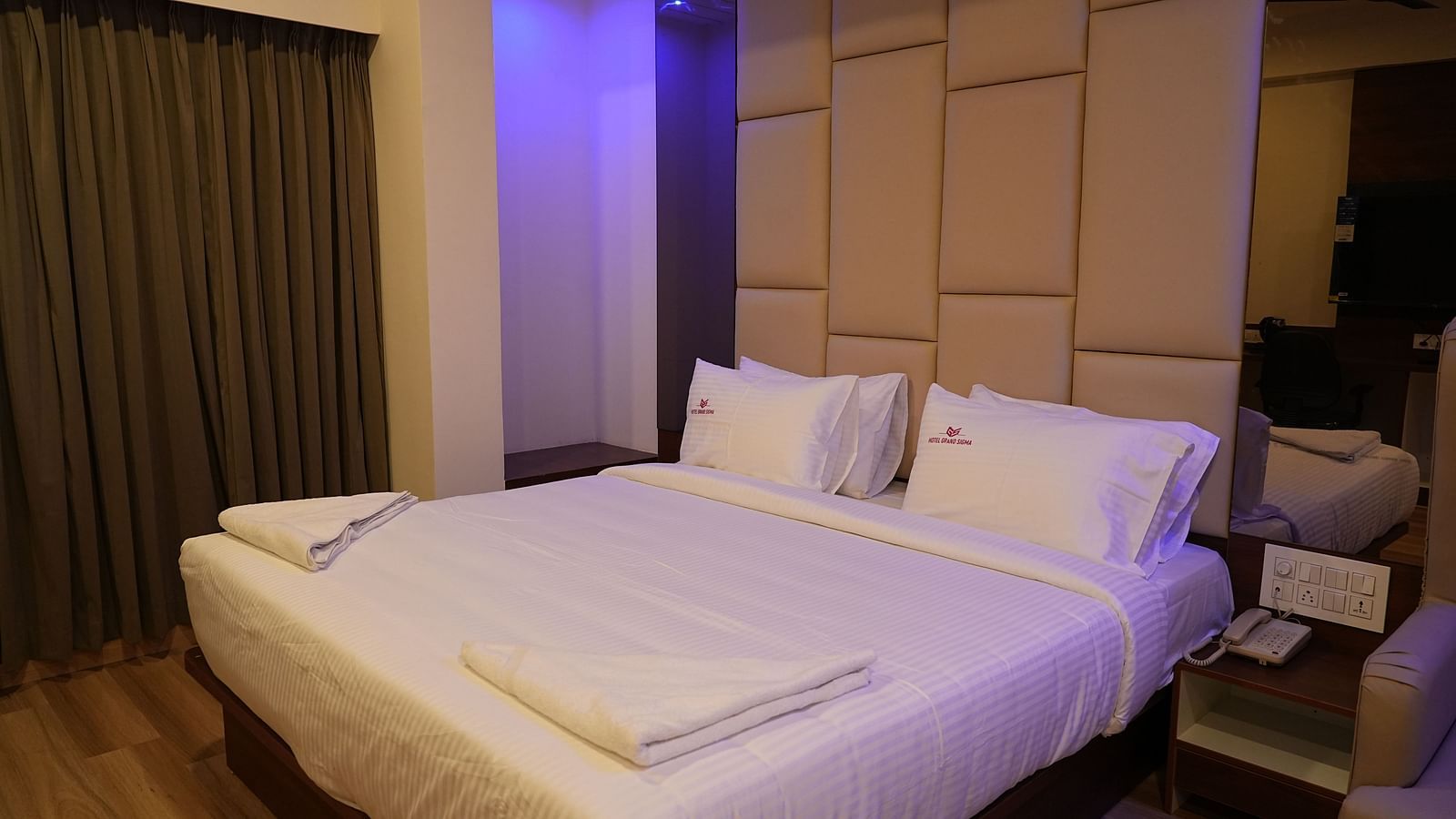 corner view of the double bed of the suite with cushioned headboard behind the bed and close curtains in the corner of the room - Hotel Grand Sigma