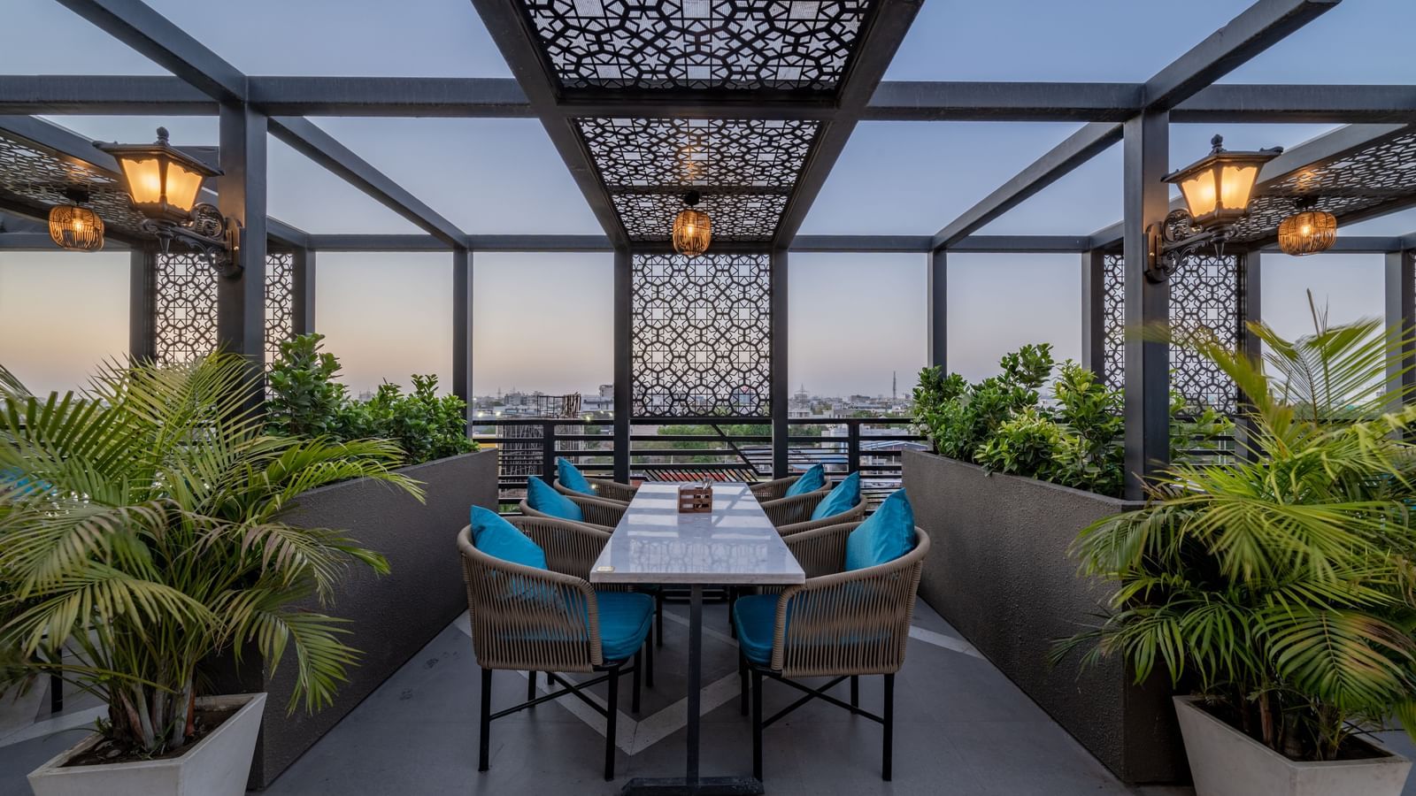 Central rooftop dining set up under decorative latticework surrounded by greenery at Hotel Highway King, Jaipur.