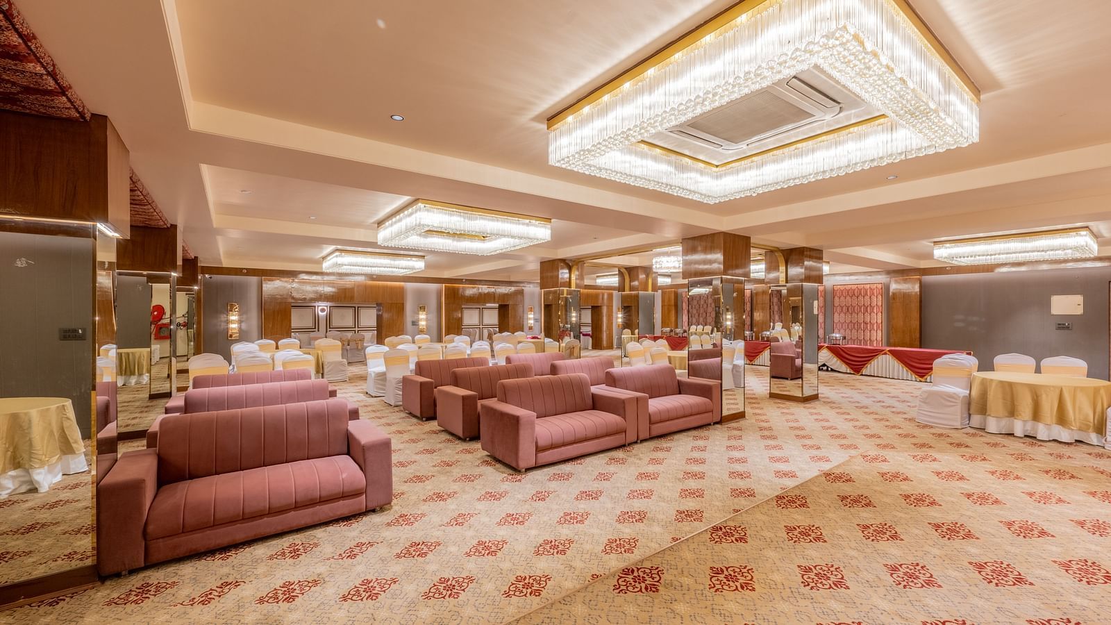 Large banquet hall with maroon sofas, chandeliers, and patterned carpet at Hotel Highway King, Jaipur.