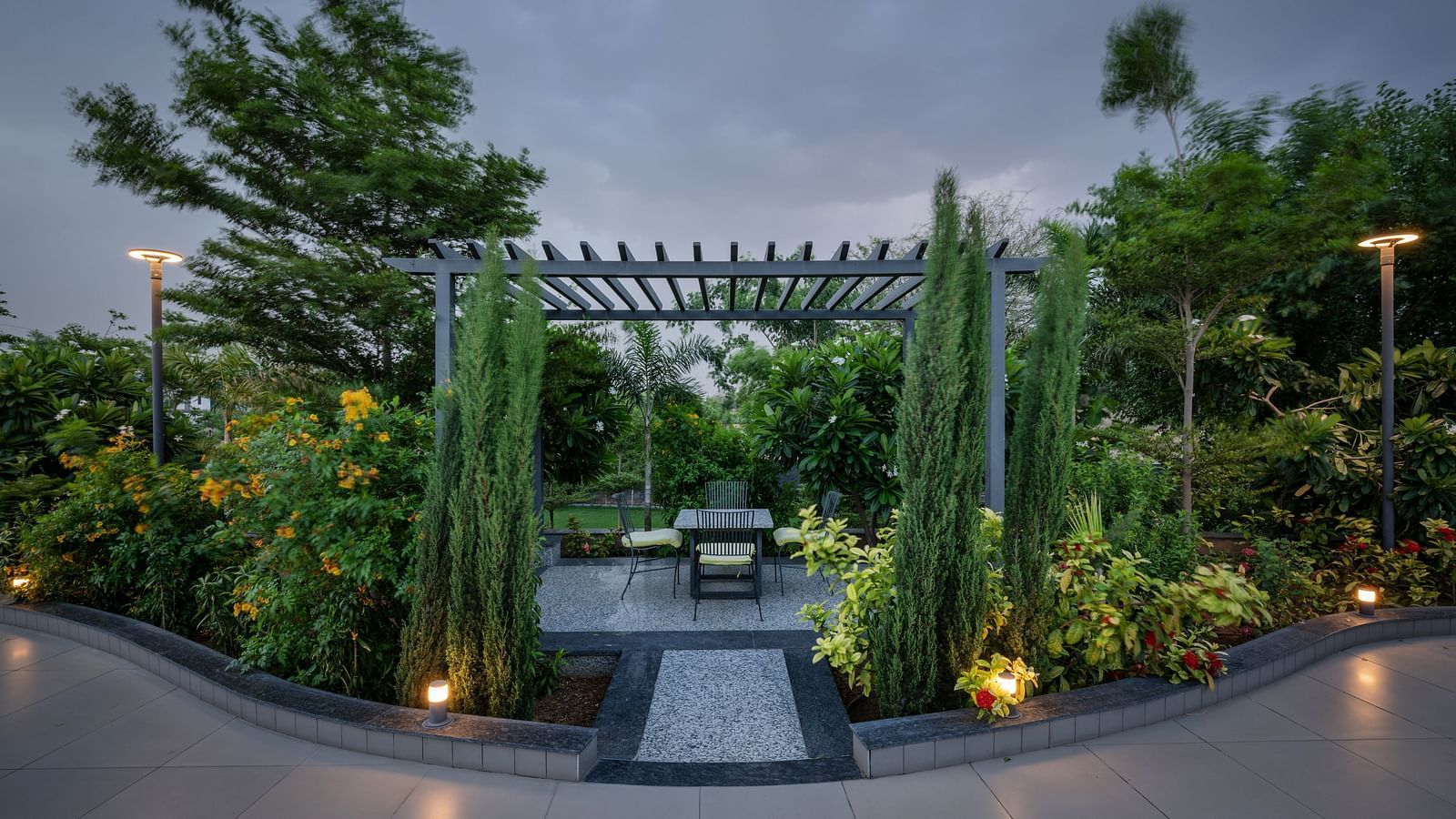 An illuminated outdoor seating area with a pergola and lush landscaping at Hotel Highway King Shahpura.