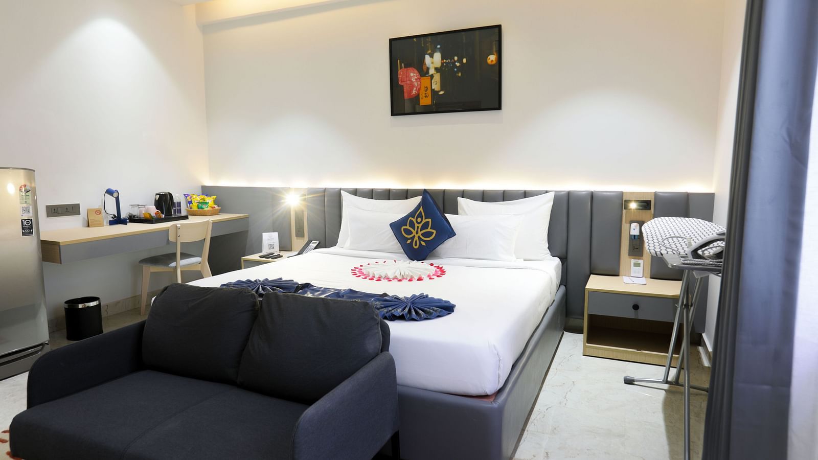 A room with king size bed, dark sofa, bedside table, framed art work on the wall and soft lighting at Hotel Kyzen HiTech City – Your Zenly Stay.