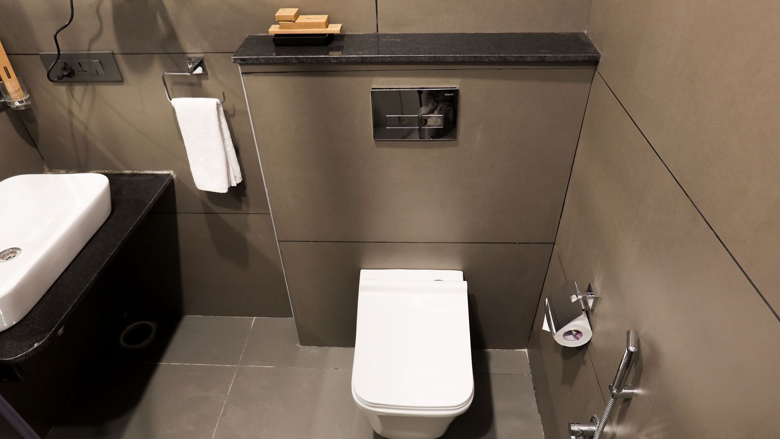 A bathroom at Hotel Kyzen HiTech City – Your Zenly Stay with sleek sink, hand shower, rolling tissue papers and wall-mounted fixtures.