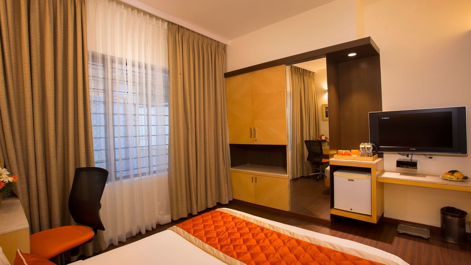 An inviting hotel room with a large window covered by sheer and opaque curtains, a wooden wardrobe and a flat-screen TV - Hotel Langford Keys by TGI, Shanti Nagar