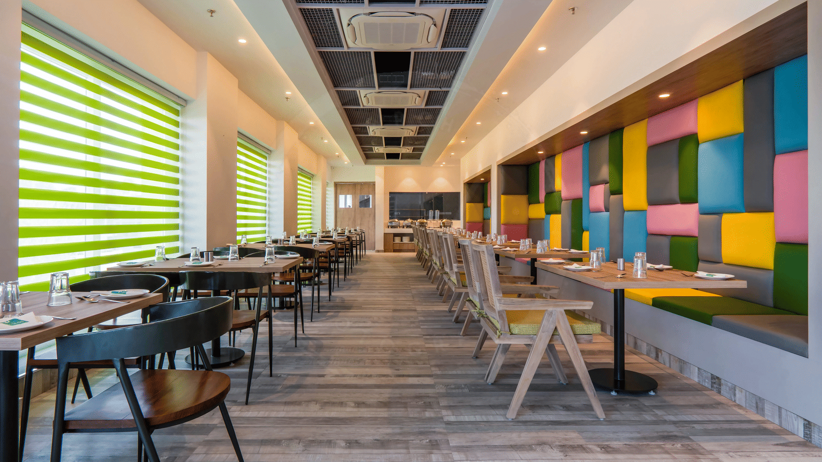 Full view of the dining area featuring a wooden floor along with colourful cushioned panels mounted on the wall at Hotel Le Roi, Dehradun.
