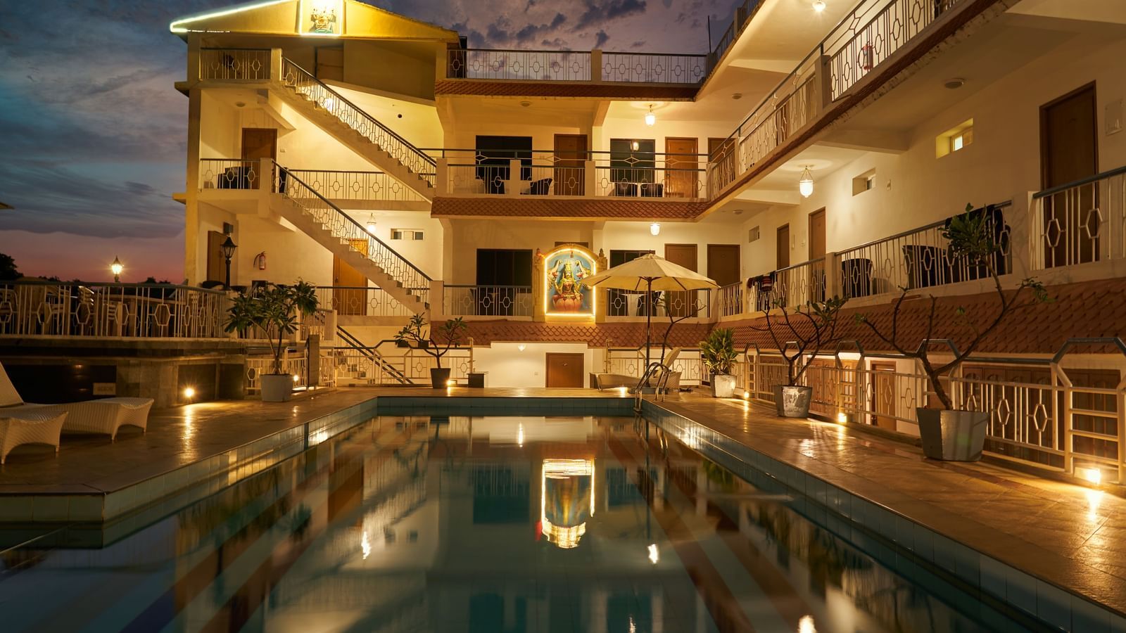 A nighttime view of Hotel Mamallaa Heritage, showcasing its illuminated facade and a beautifully lit swimming pool reflecting the lights.