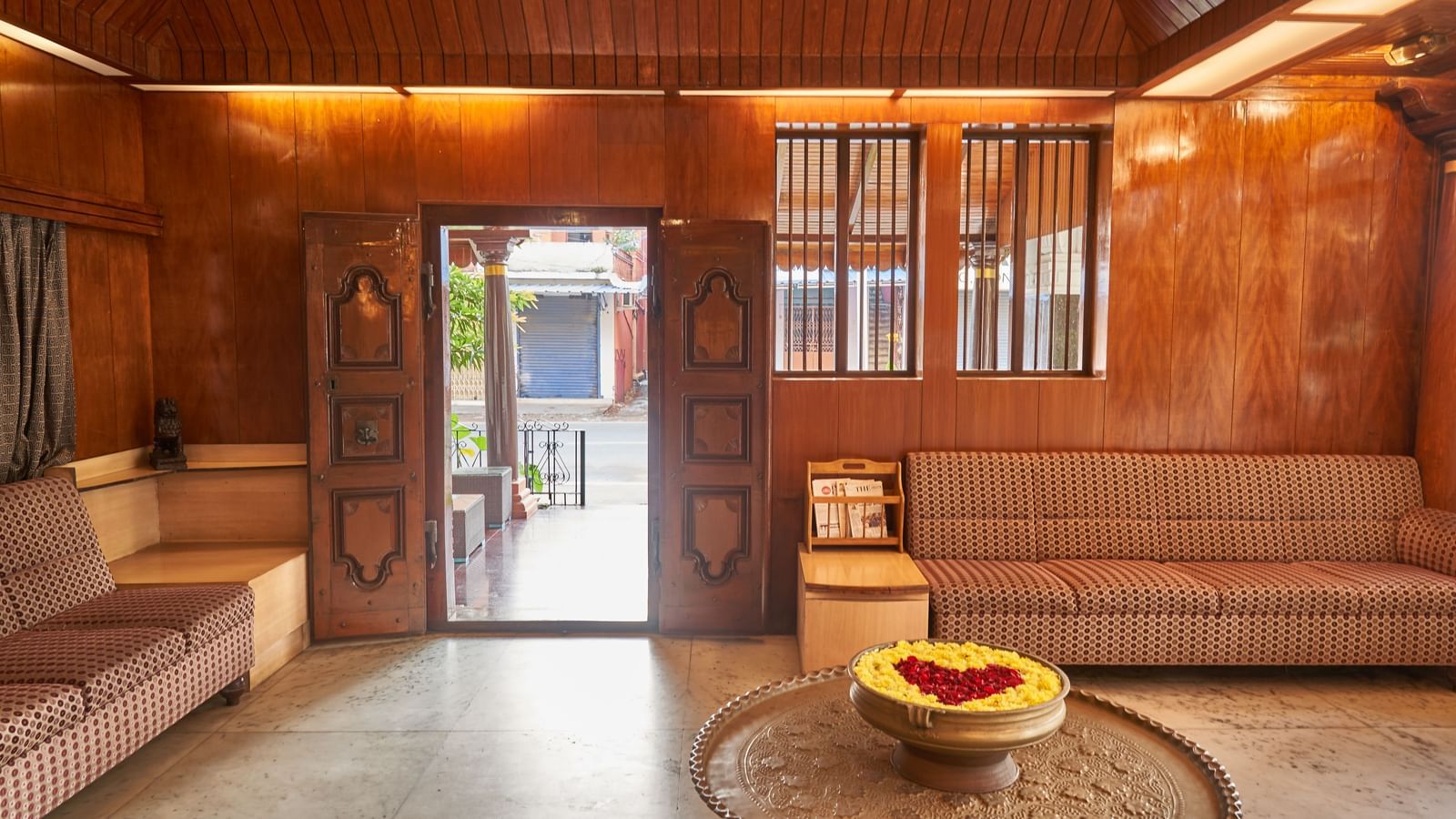 A warmly lit interior space at Hotel Mamallaa Heritage, showcasing a grand wooden doorway, traditional decor, and a low table with a decorative bowl.
