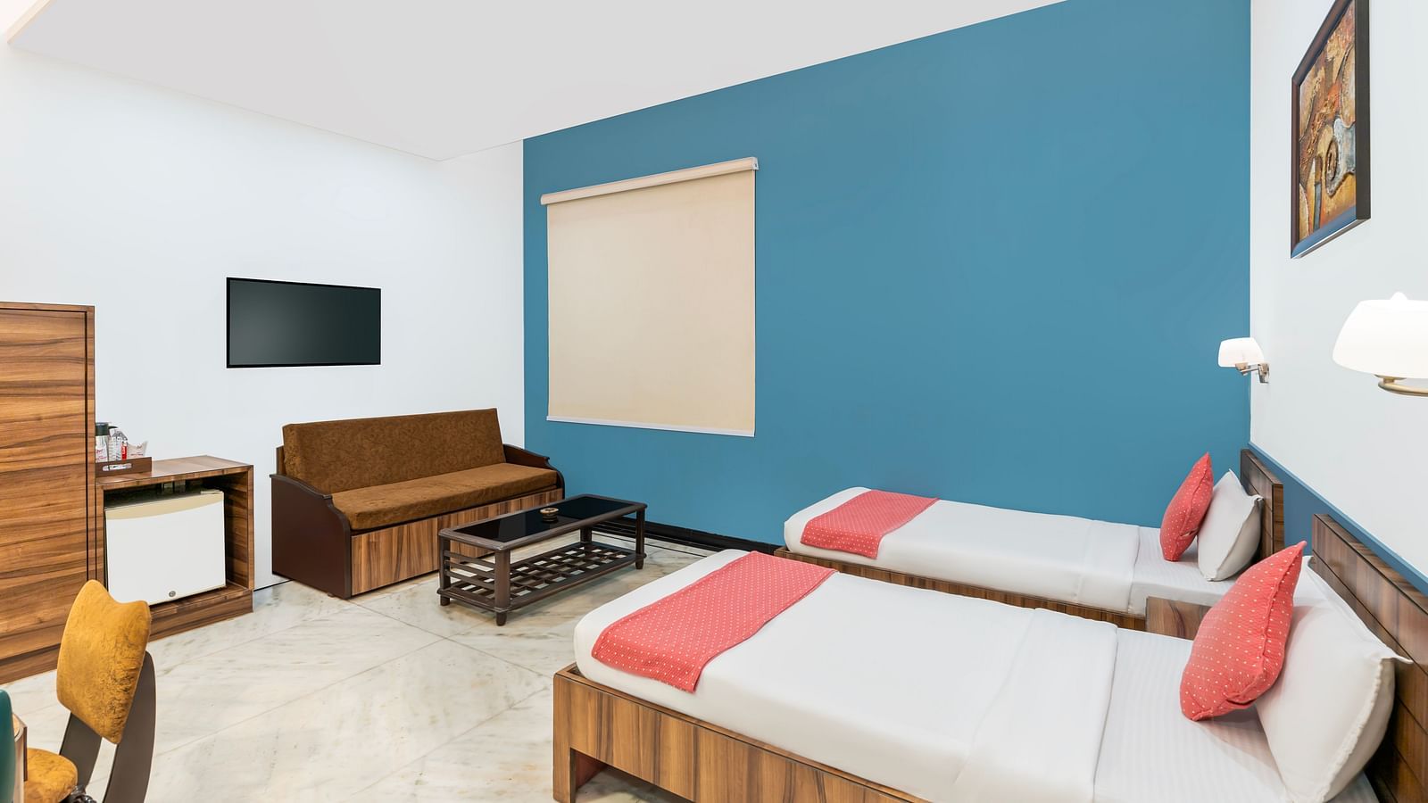 A corner view of the room at Hotel Moti Palace, featuring twin size beds, a sofa, and a flat-screen TV.