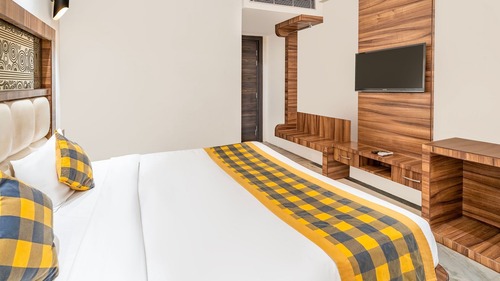 A side angle view of the bedroom at Hotel Moti Palace, featuring a comfy bed, a work desk, and a flat-screen TV.