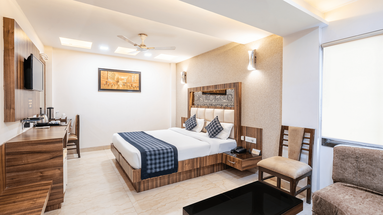 A side view of the room at Hotel Moti Palace, featuring a comfy bed, a chair, and a tea table.
