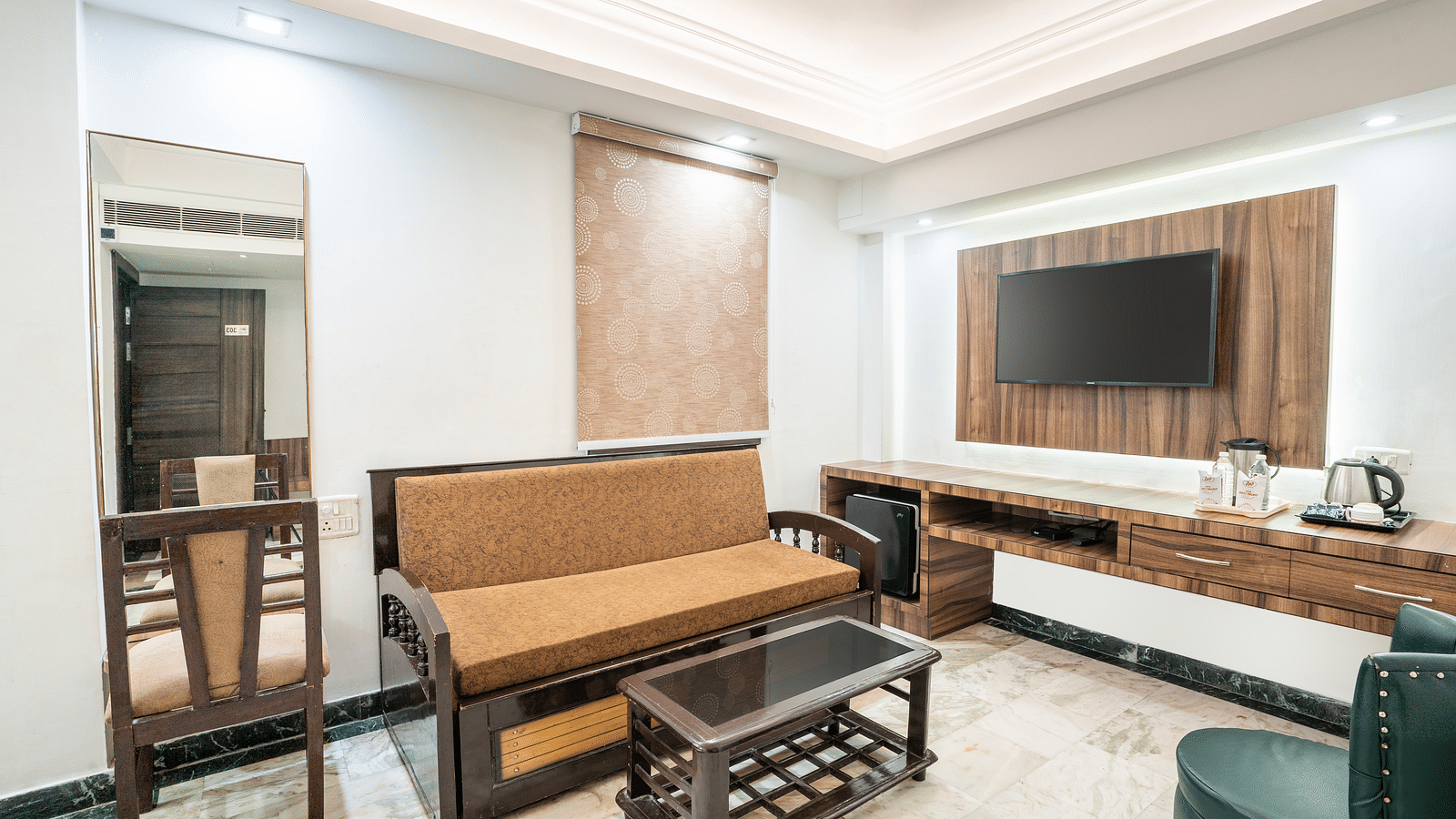 An image of the living area at Hotel Moti Palace, featuring a comfy sofa, a chair, a tea table, and a flat-screen TV, creating a cozy and inviting atmosphere.