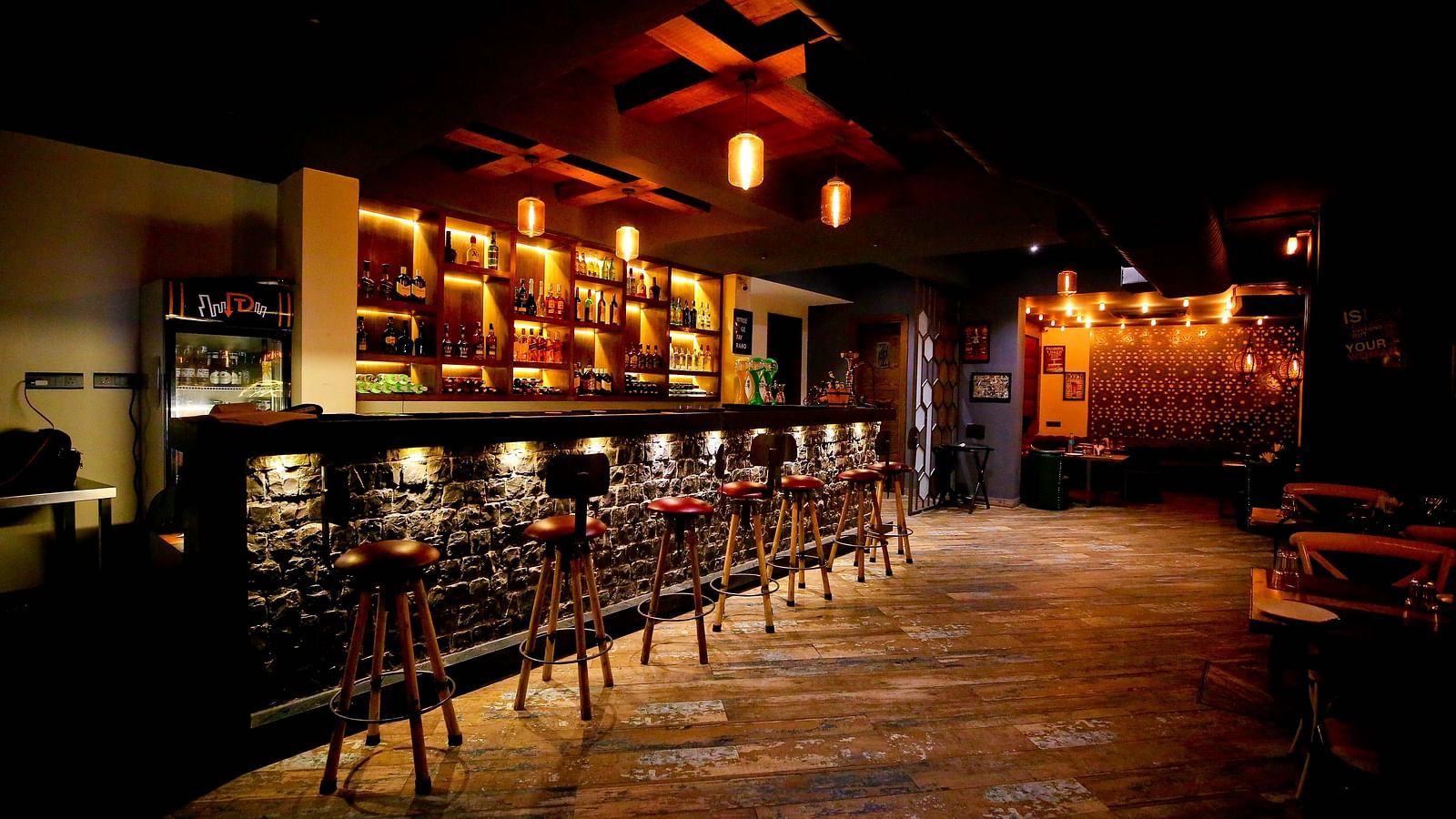 A rustic-themed bar counter lined with stools in a softly illuminated dining space - Hotel Moti Palace, best hotel near Agra Fort