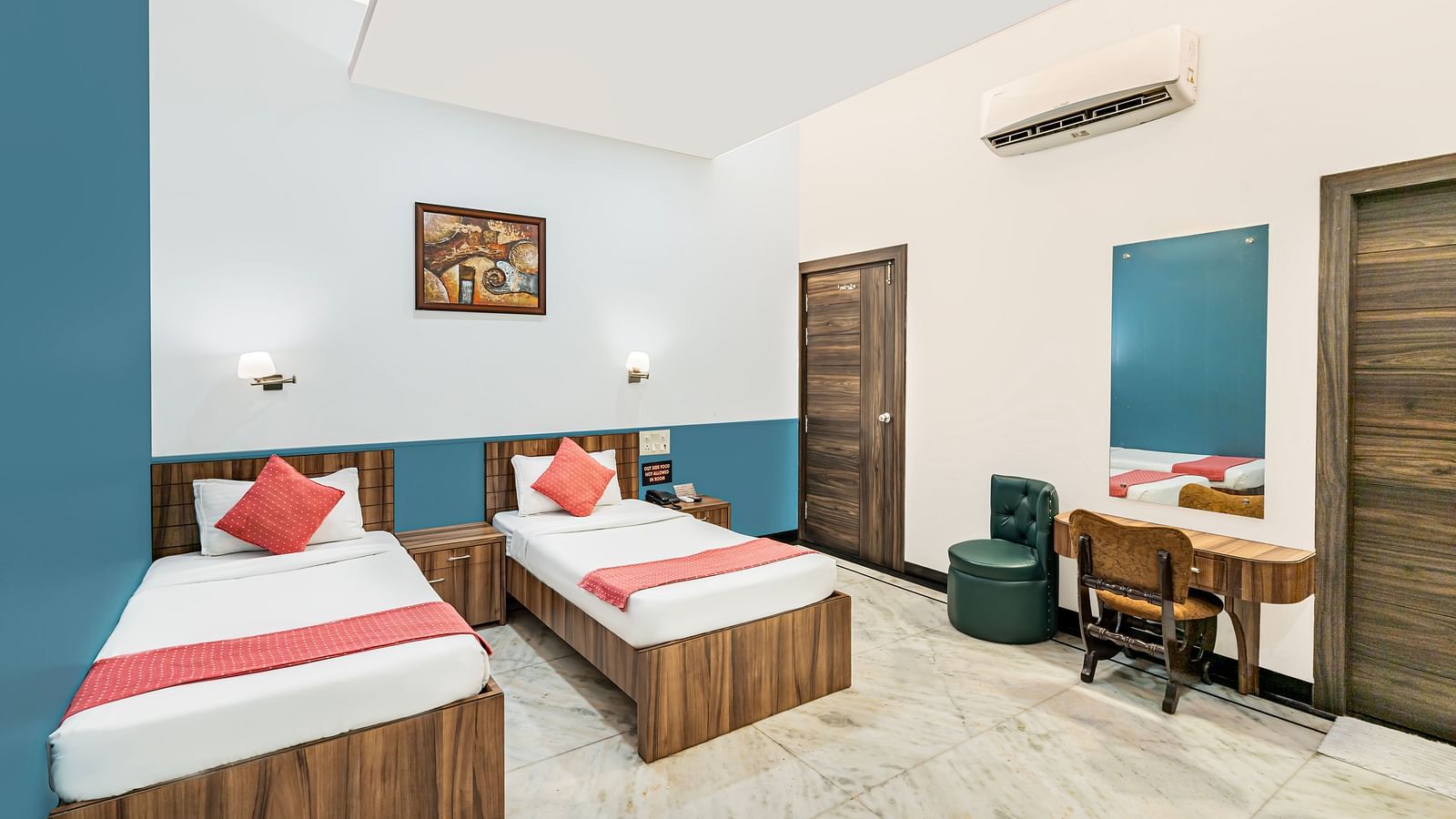 A corner view of the room at Hotel Moti Palace, featuring twin-size beds and a work desk.