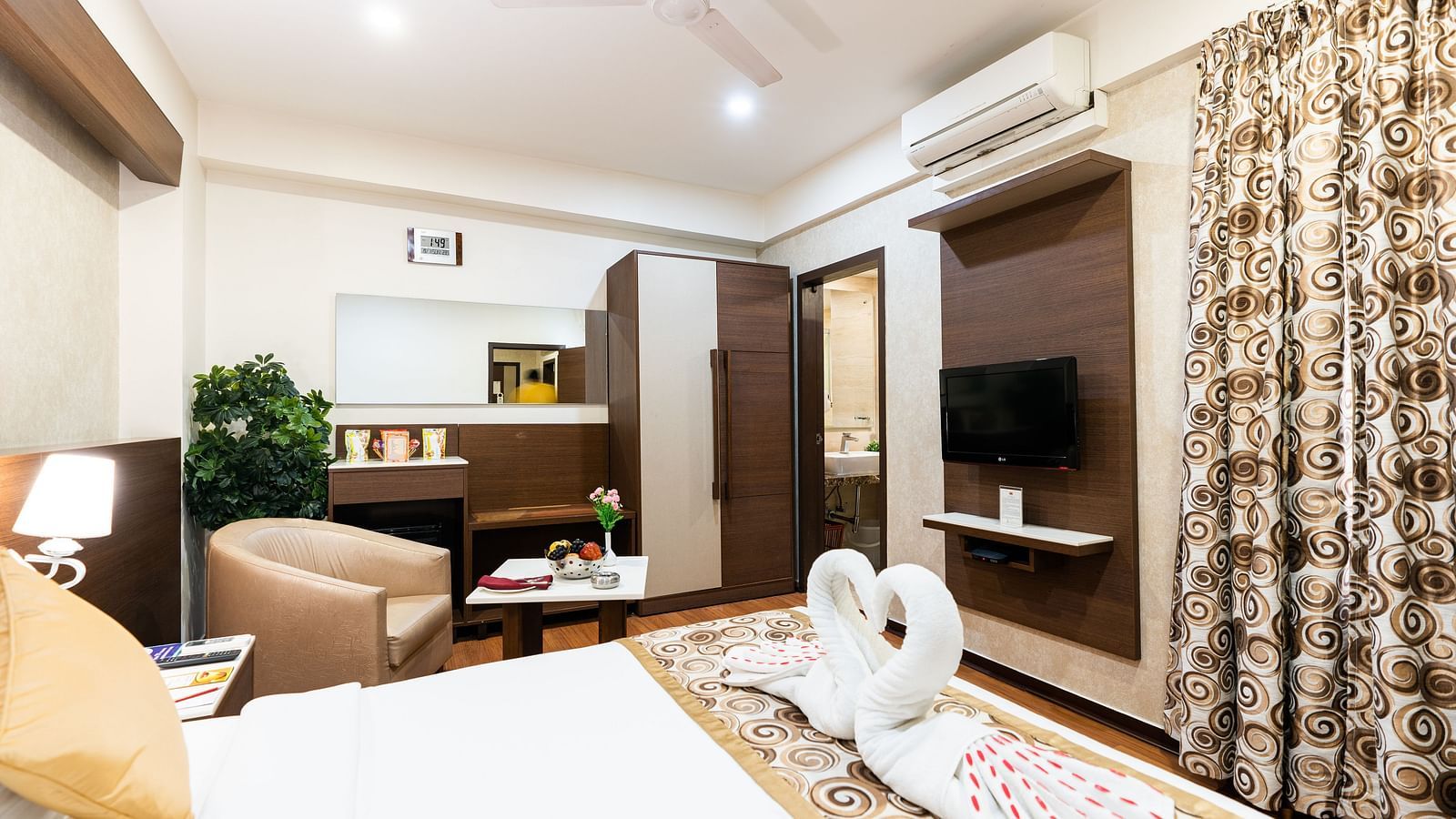 a double bed with a sofa and table next to it and a wall mounted tv opposite it - Hotel Pai Vista, Mysore
