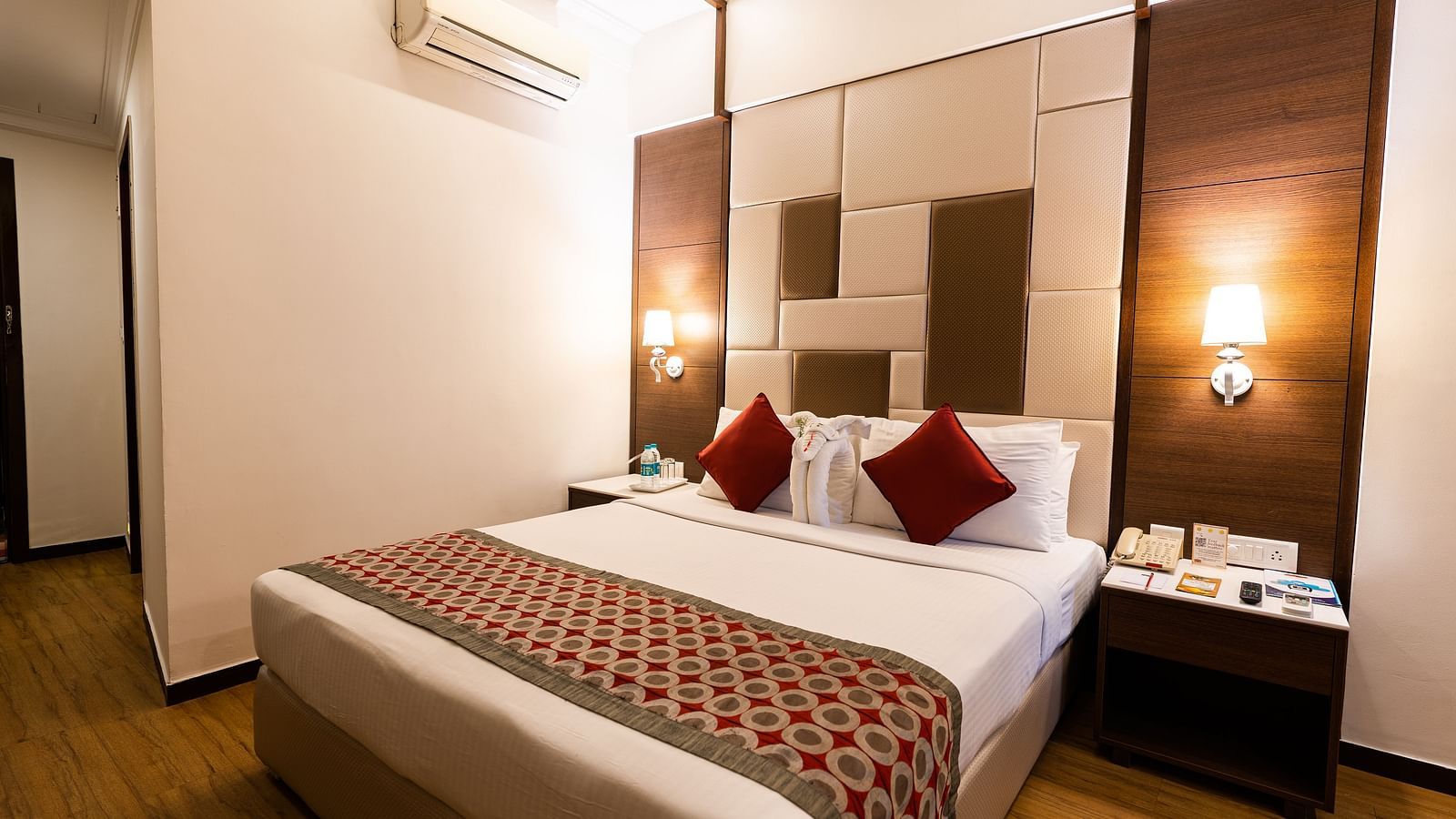 a double bed with red runner and pillows on it and an ac wall mounted inside one of the rooms - Hotel Pai Vista, Mysore