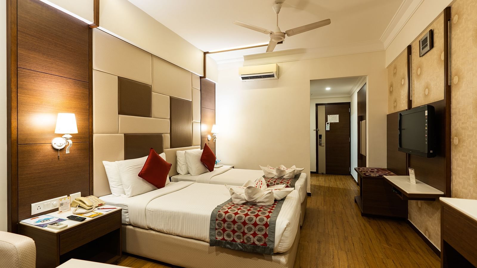twin beds with a tv wall mounted opposite it inside one of the rooms - Hotel Pai Vista, Mysore