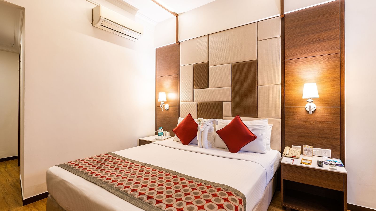 a double bed with red pillows and runner with side tables inside one of the rooms - Hotel Pai Vista, Mysore