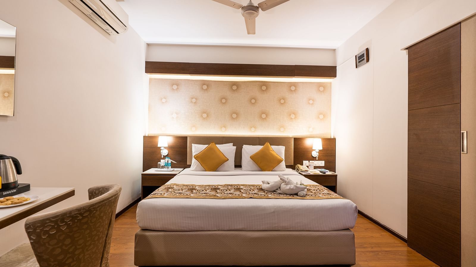 a double bed with a fan hung above it and an AC next to it inside one of the rooms - Hotel Pai Vista, Mysore