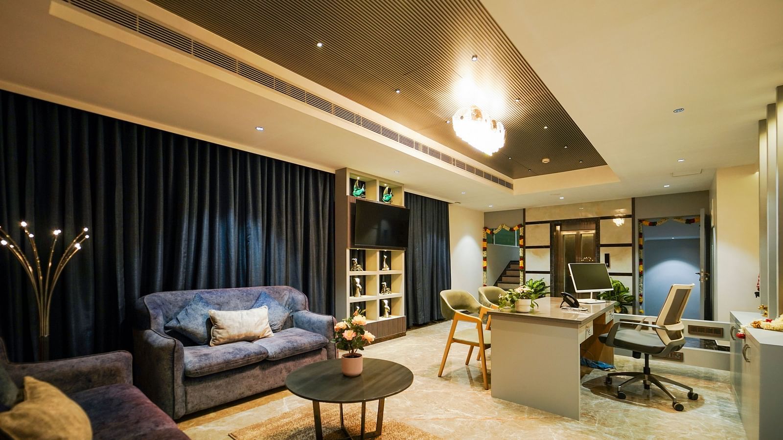 A hotel suite living space includes sofas, a round table with flowers, a television, and a work desk with chairs - Hotel Park Inn, Nellore.