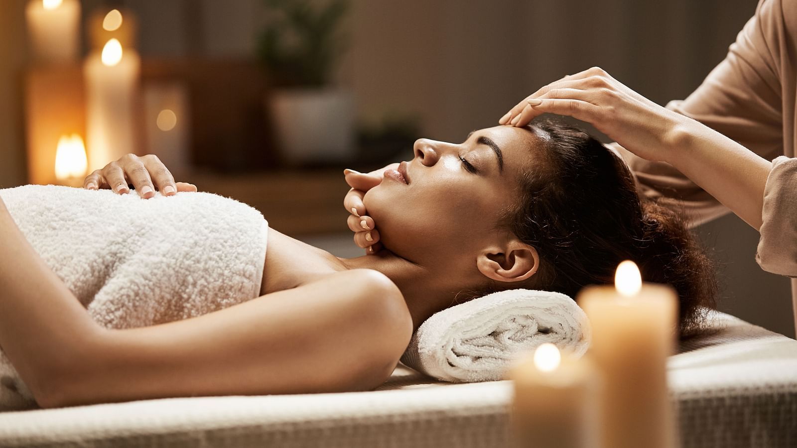 A woman lying down on a spa table with a masseuse massaging her face - Hotel Rajdarshan, Udaipur.