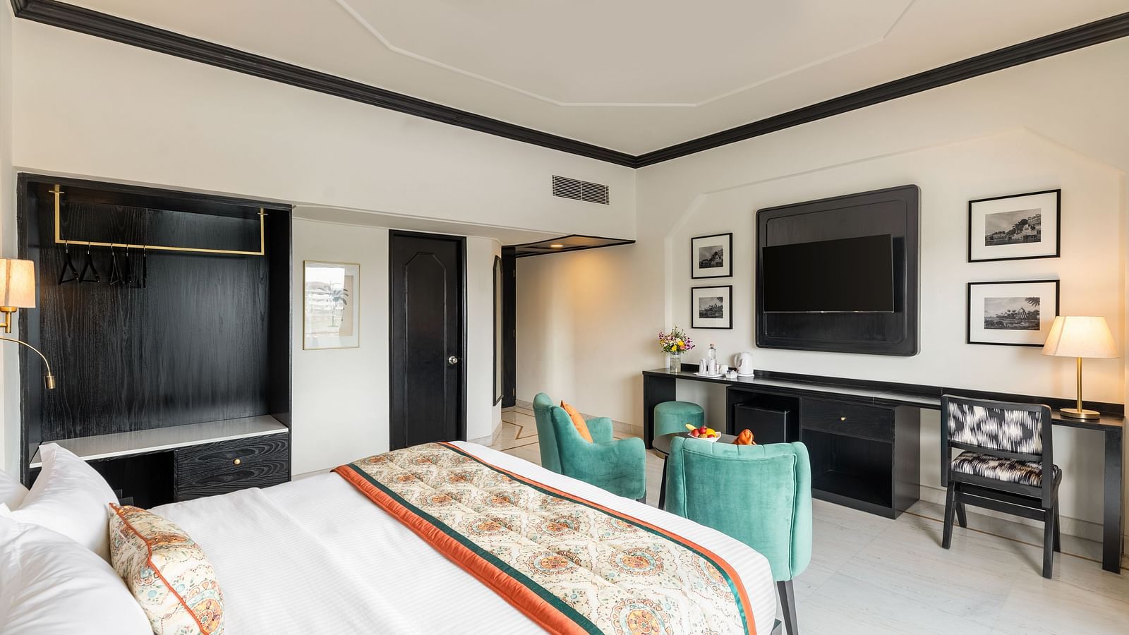 a king size bed in a spacious hotel room in Udaipur featuring two green armchairs, a TV, a wardrobe and several wall paintings - Hotel Rajdarshan, Udaipur.