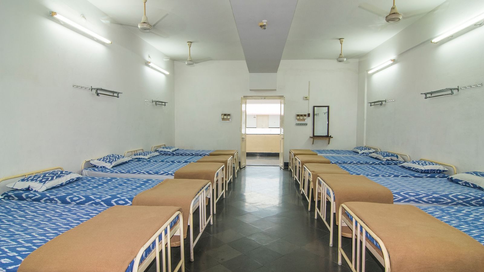 A full view of beds with bedding arranged in two rows in a room | Hotel Sahara
