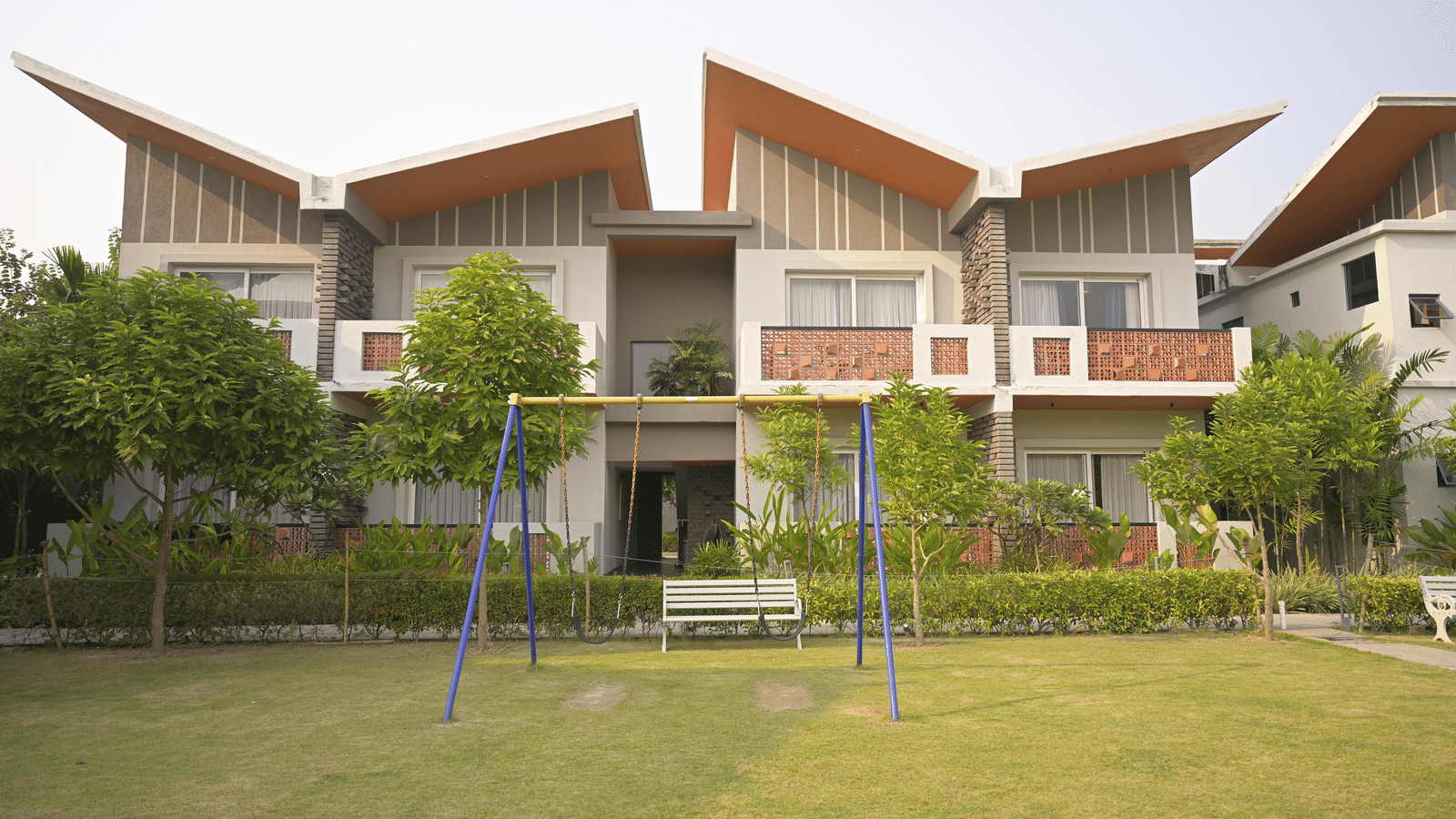 A wide view of the outdoor children’s playground with swings and a lawn in front of the Hotel Sonar Bangla Mayapur.