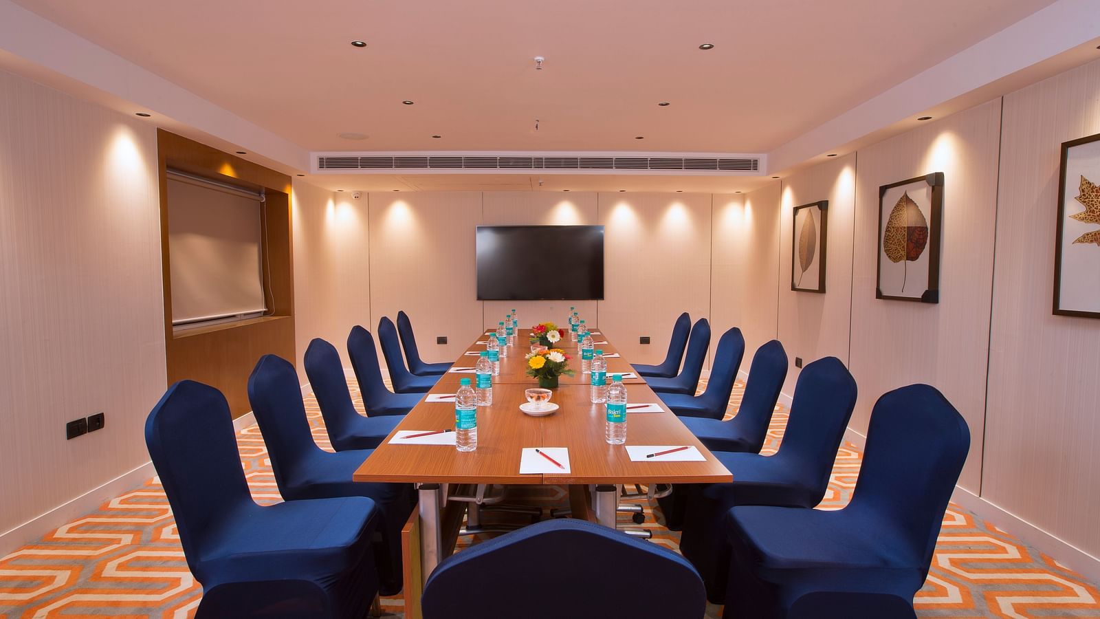 A well-lit boardroom with a long table, blue chairs and a large screen on the wall, suitable for business meetings - Hotel Southend by TGI - Bommasandra, Bangalore