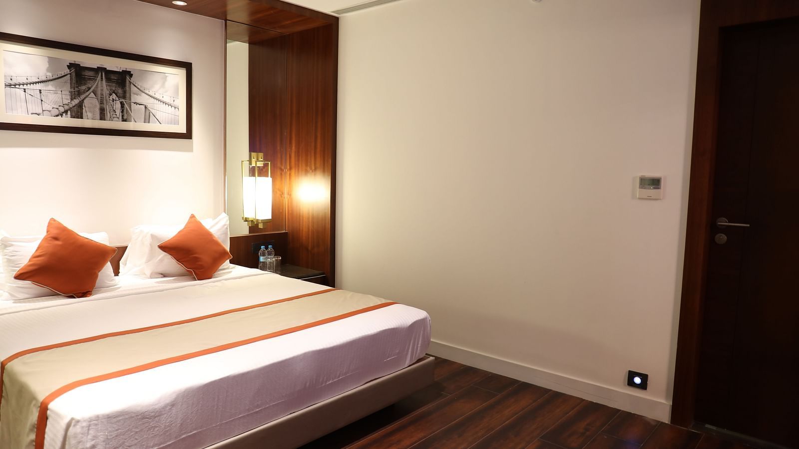 A hotel room with a large bed, white linens, burnt orange accents and a framed picture of a bridge above the headboard - Hotel Southend by TGI - Bommasandra, Bangalore