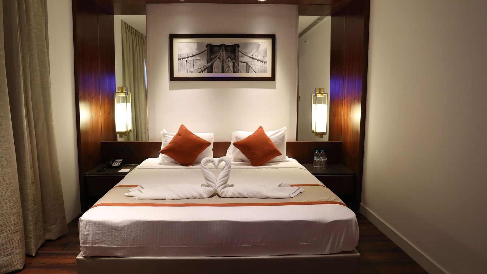The front view of a hotel room with a large bed, white linens, burnt orange accents and a framed picture of a bridge above the headboard - Hotel Southend by TGI - Bommasandra, Bangalore