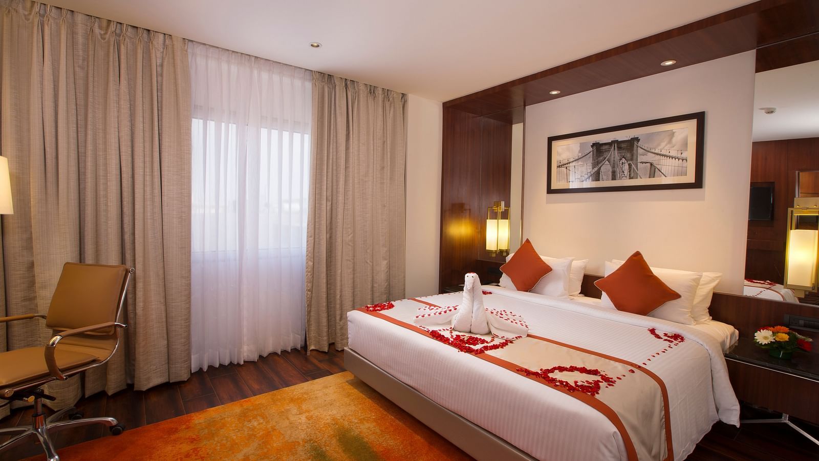 A hotel room with a large bed with white and orange linens, a brown office chair and sheer curtains over a window - Hotel Southend by TGI - Bommasandra, Bangalore