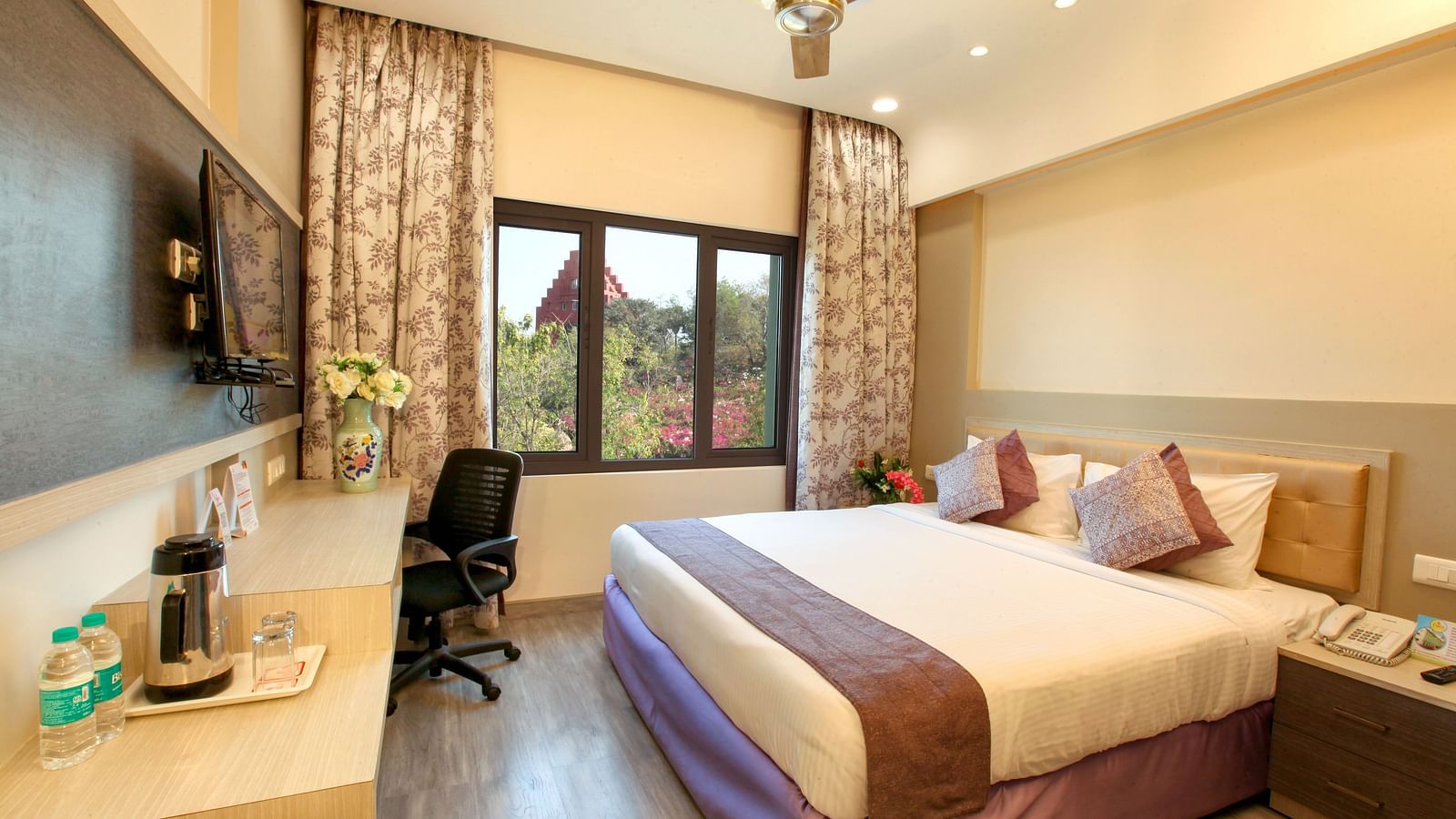 A spacious and elegantly decorated hotel room with a large window and a work area. - Tara, Comfort Hotel in Hyderabad - Ramoji Film City.