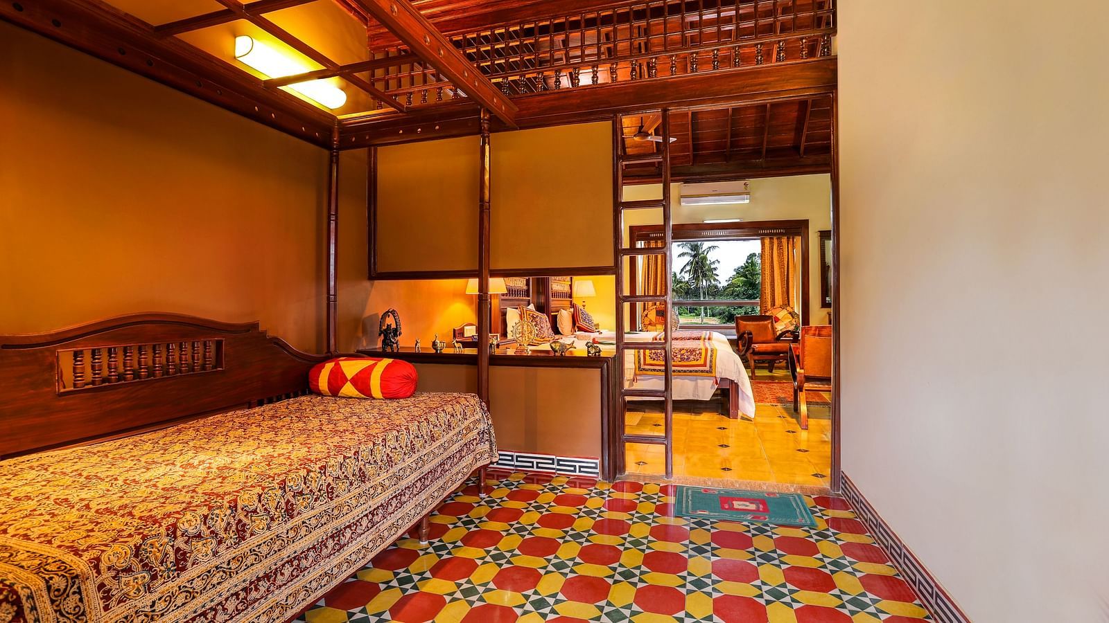 An image of bedrooms where one bed just has a bolster pillow while the other bedroom has decorative items, seating area, and other amenities -  Hoysala Village Resort, Hassan