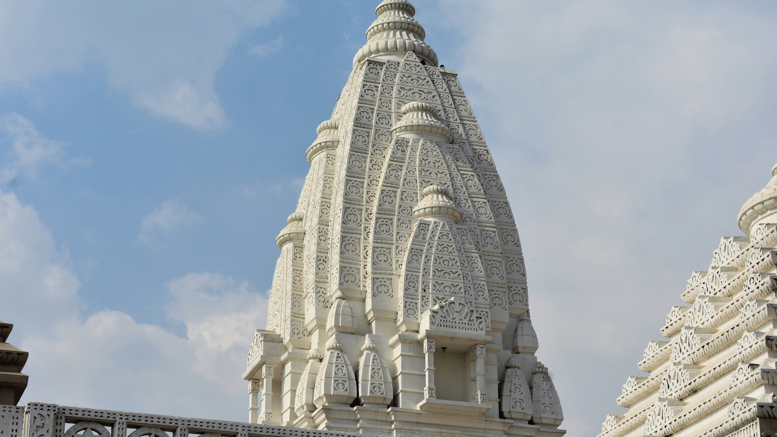 A view of a dome of a jain temple from below with white clouds on blue sky in the background.