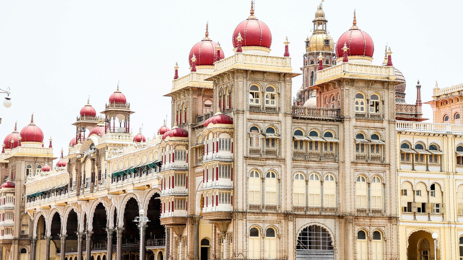 Front view of the grand Mysuru palace with three-storeys and pink domes with arched facades.