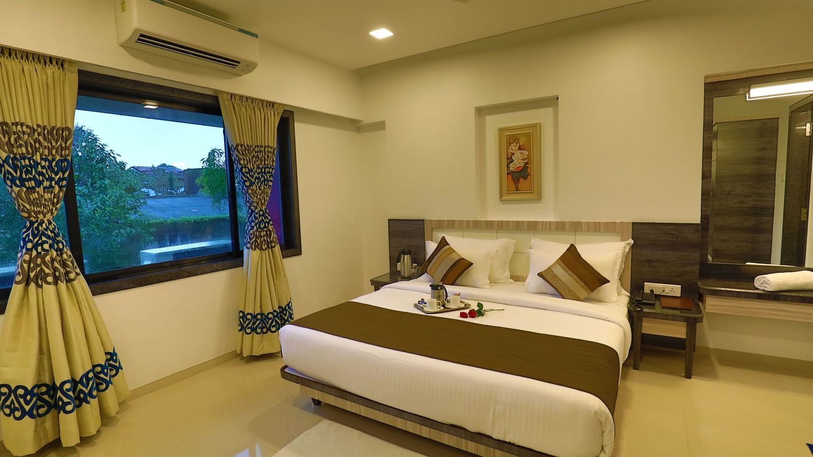 A suite at Imperial Grande with a well-made bed and a window with patterned curtains.