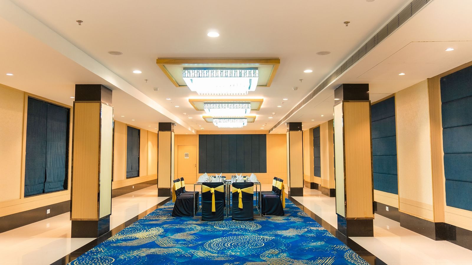 a hall with a table surrounded by decorated chairs and overhead lighting - Jardin Hotels
