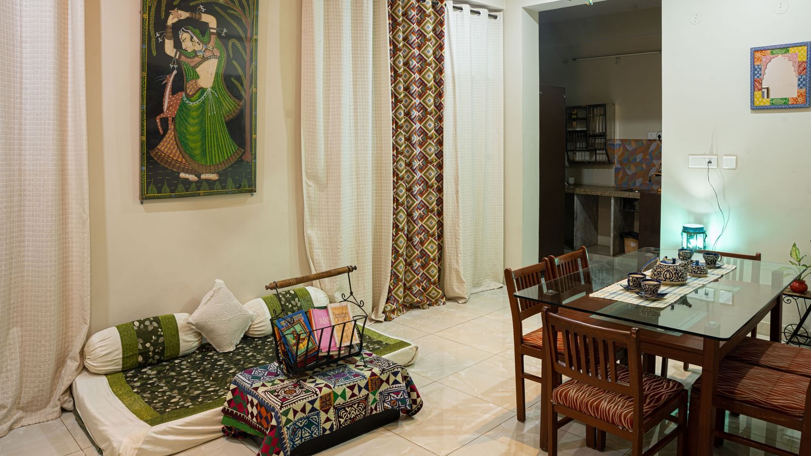 Indoor living space with low seating, dining table, wall painting, and curtains at Jaypore360 Homestay in Jaipur.