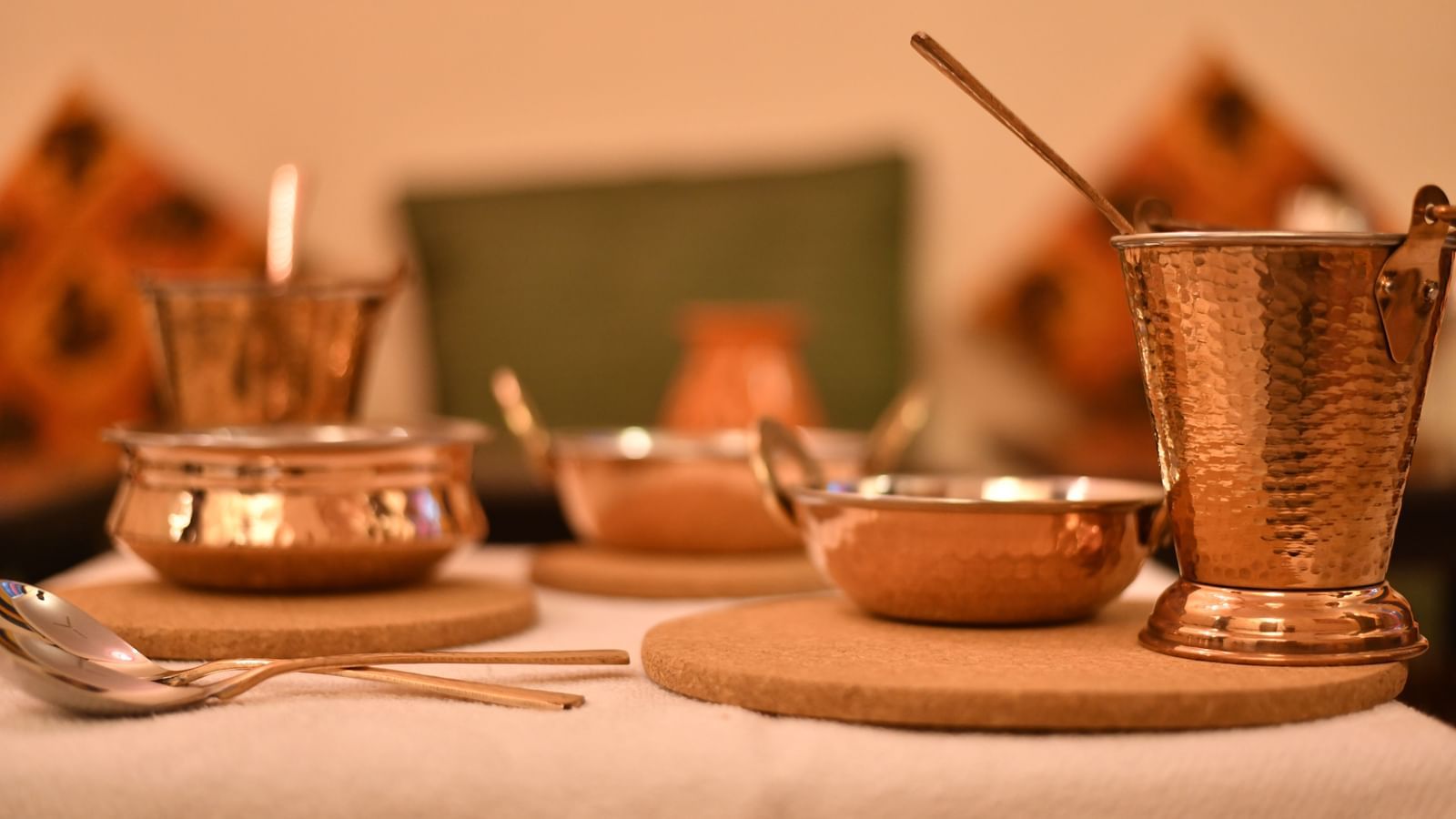 A close-up of traditional dining utensils including cups, plates, and ladles on a set dining table at Jaypore360 Homestay in Jaipur.