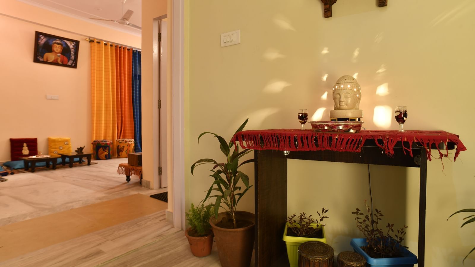 A small indoor shrine with lit lamps, plants, and decorative items arranged on a wall-mounted shelf at Jaypore360 Homestay in Jaipur.