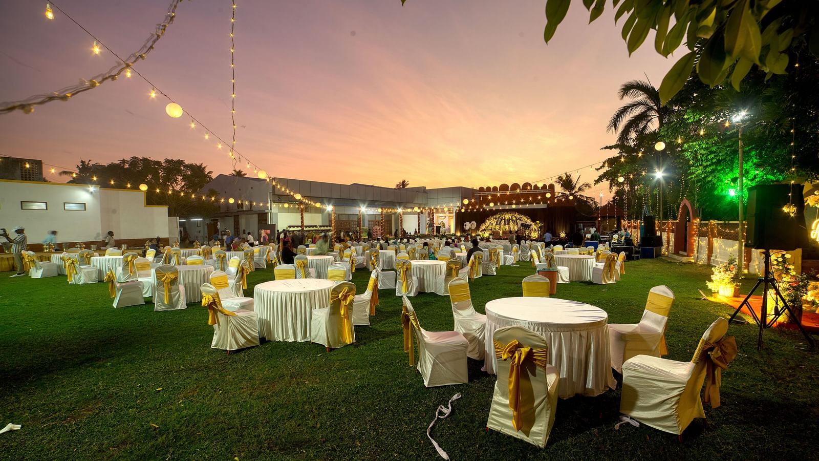 Elegant lawn event arrangement with round tables and ambient evening lighting at Kailash Conventions ECR.