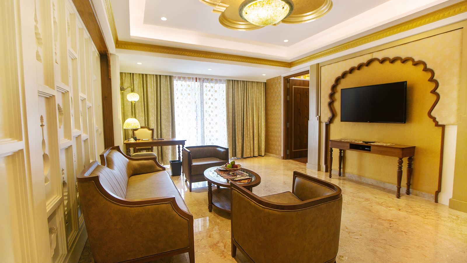 The living room of Executive Palace Suite featuring a coffee table surrounded by couches, a television, and a wall-mounted flat screen television - Kaldan Samudhra Palace