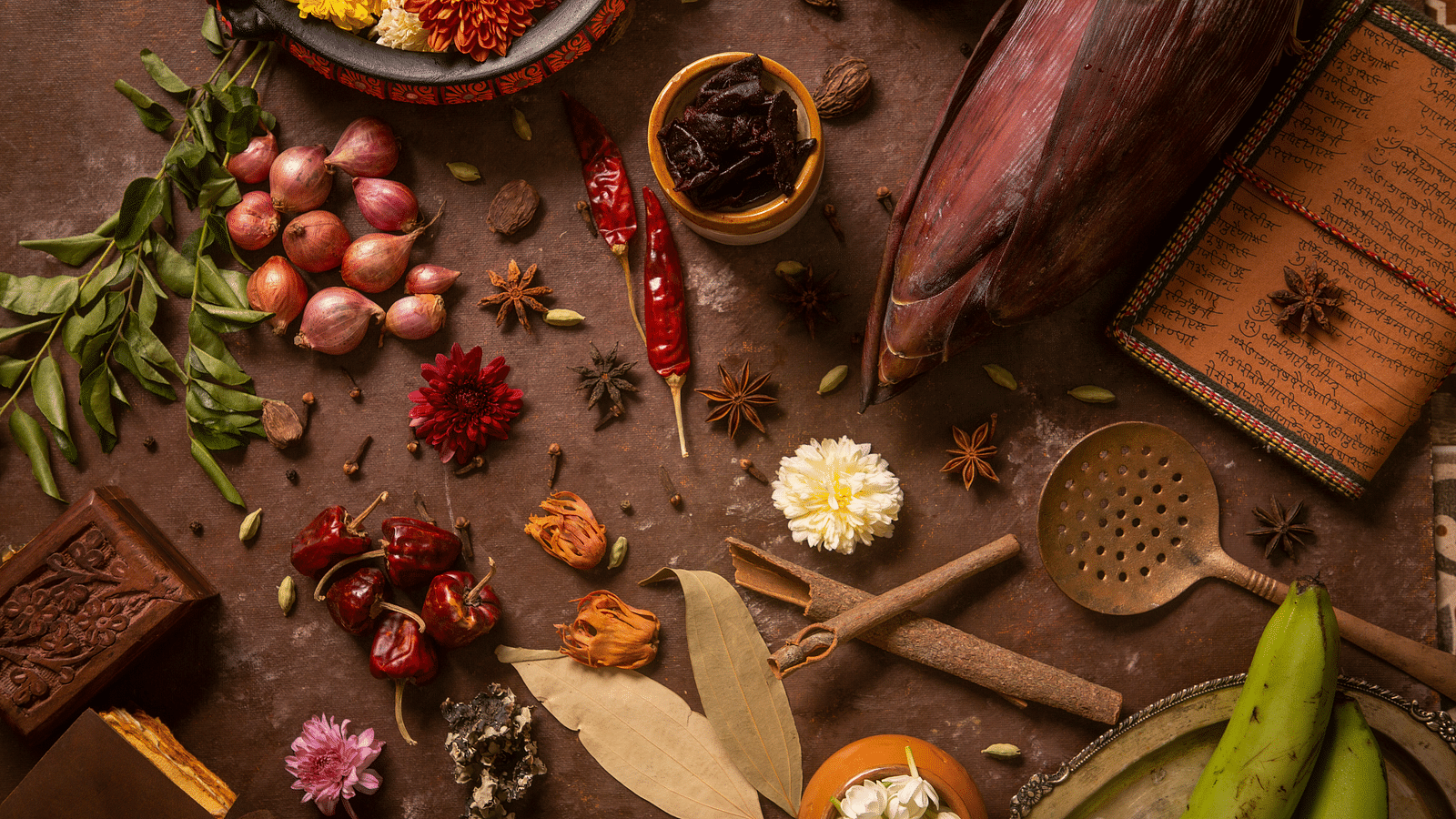 Assorted spices and kitchen tools beautifully arranged with flowers and vegetables on a rustic background | Kamats India